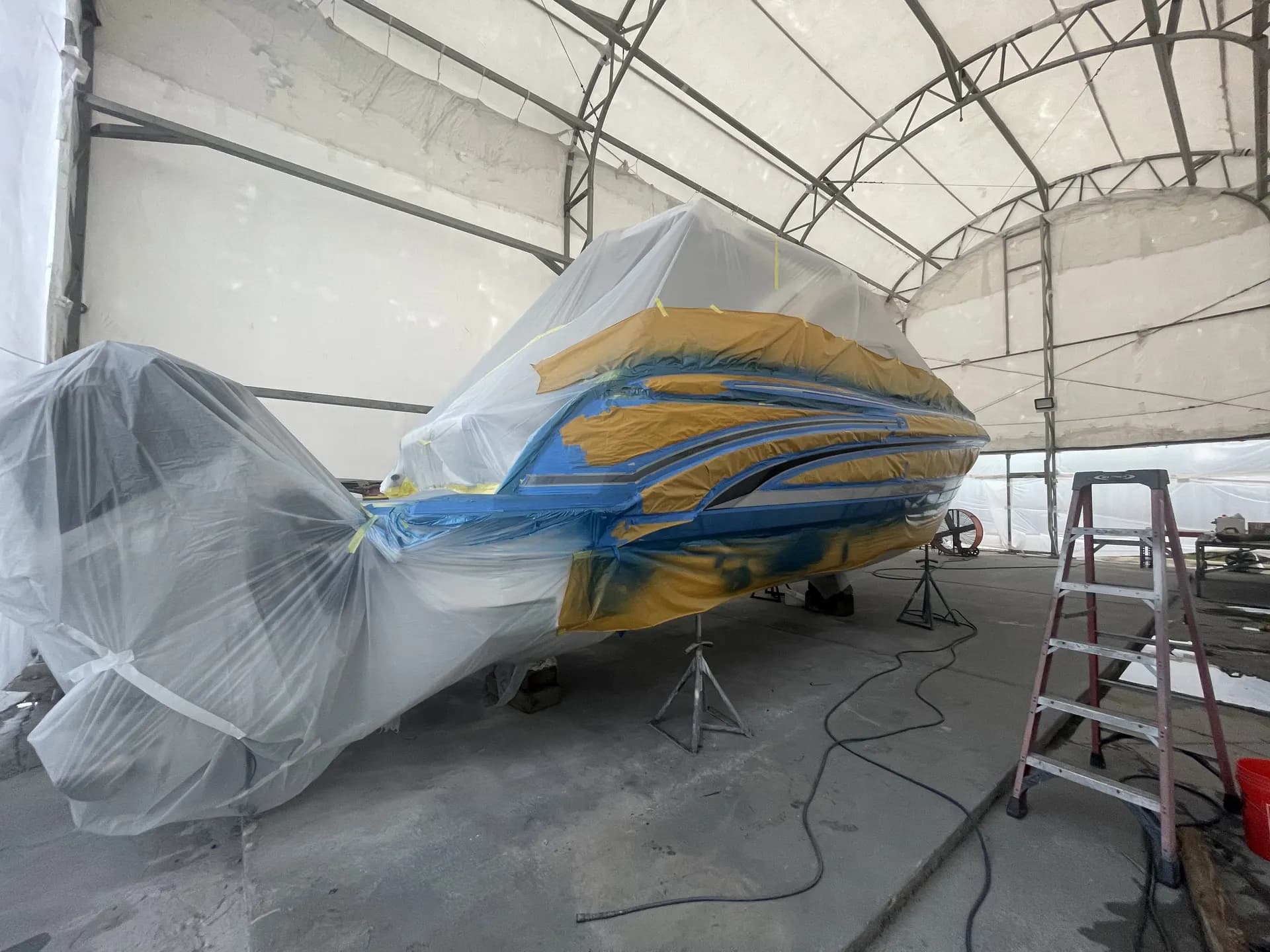 Stern-quarter view of a powerboat under plastic and tape masking during refinishing