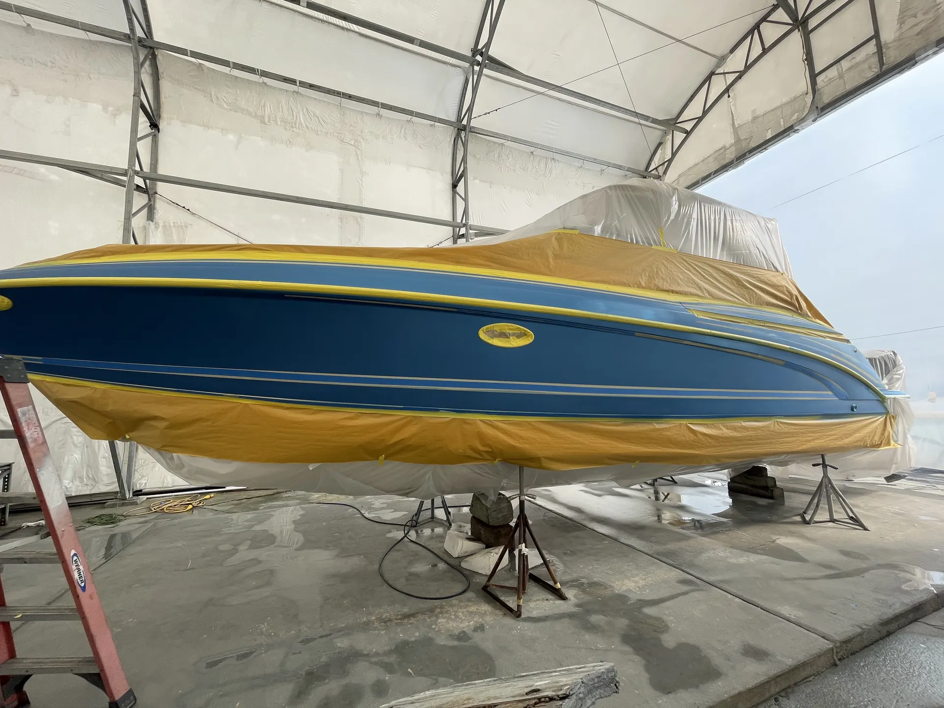 Navy hull under protective masking paper inside a controlled marine coating enclosure