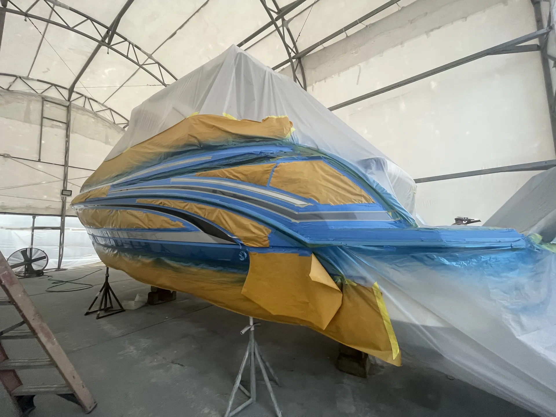 Protective plastic showing overspray while a hull is masked during marine coating work